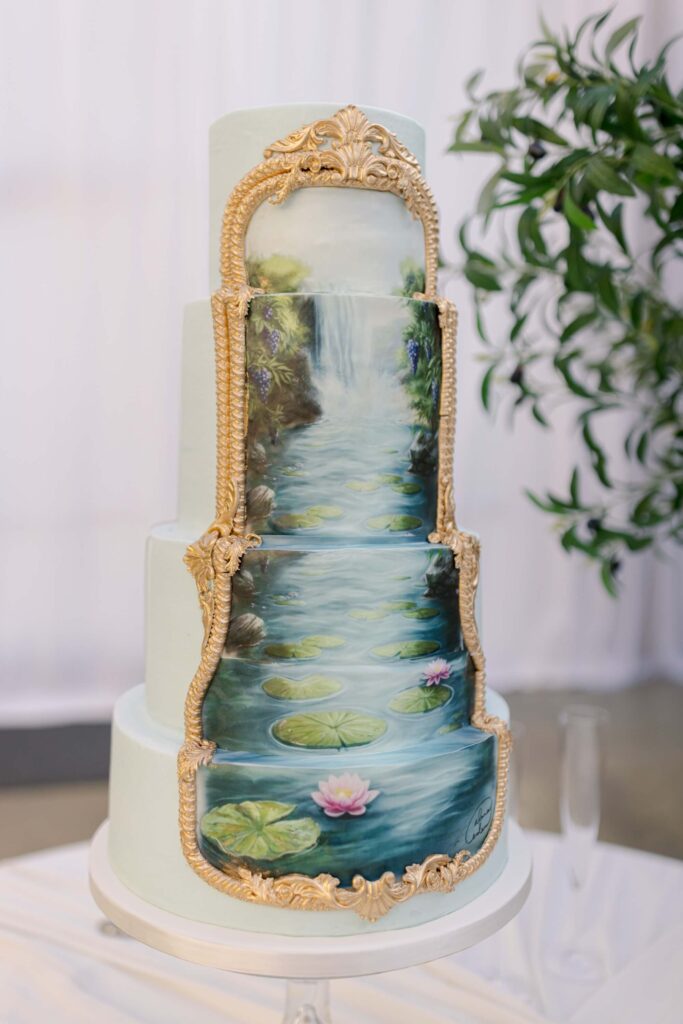 Four-tier wedding cake featuring a reproduction of an original French Impressionist style landscape painting by artist Alana Eden of Eden Hill Atelier, framed in ornate gold molding.⁠